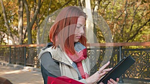 Girl with foxy hair stands outdoors in sunny weather use tablet and makes an online order