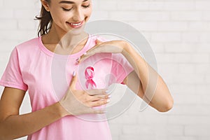 Girl Framing Pink Ribbon On T-Shirt Standing Against White Wall