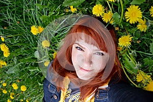 Girl with freckles red-haired young woman lying on the grass on a dandelion field