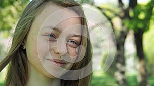 The girl with freckles smiles. Face of a teenager close-up. A girl with blue eyes and freckles in the fresh air.