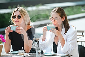 Girl friends in cafe outdoor. Two beautiful girls with cups coffee in summer cafe. Outdoors portrait of two young