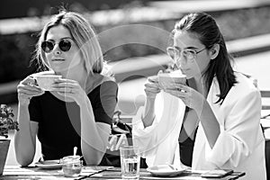 Girl friends in cafe outdoor. Two beautiful girls with cups coffee in summer cafe. Outdoors portrait of two young