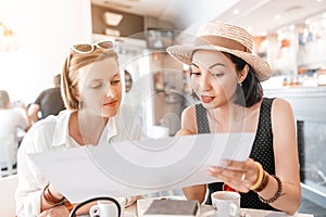 Girl friends carefully read menu, sitting in a cafe. Small business and dining room concept
