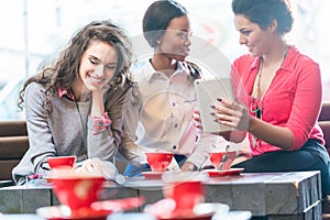 Girl friends sitting together in cafe and showing photos on smar