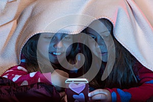 Girl friends under blanket playing with mobile phone