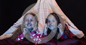 Girl friends watching TV in blanket tent. Pyjamas party