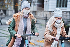 Girl friends wearing face masks and commuting on scooter in the city