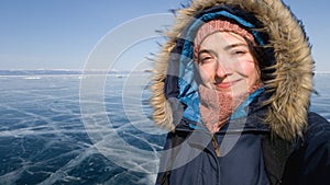 A girl on a frosty clear day takes a selfie on the ice of lake Baikal. Girl in warm coat and hood