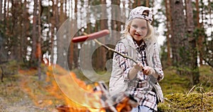 girl frying sausage over bonfire in forest. outdoor adventures