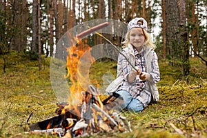 girl frying sausage over bonfire in forest. outdoor adventures