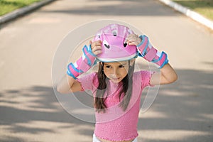 A girl in full protective gear puts on a helmet before riding a bike