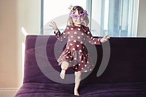 Girl with funny glasses jumping dancing on couch indoors