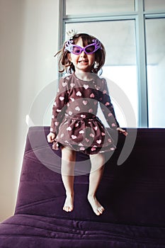 Girl with funny glasses jumping dancing on couch indoors