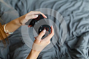 Girl gamer playing video game with wireless joystick at home. Gamepad in female hands close-up, gaming addiction concept, woman