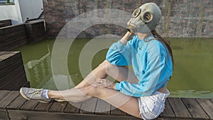 A girl in a gas mask sits by the fountain. Alienation in the city. Fashion, ecology and loneliness concepts