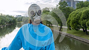 A girl in a gas mask stands on a bridge across the river. Alienation in the city. Fashion, ecology and loneliness concepts