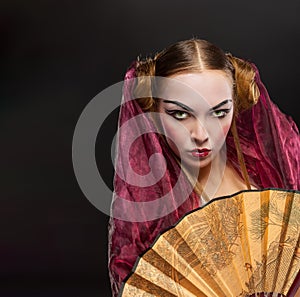 Girl in geisha costume with fan on black background