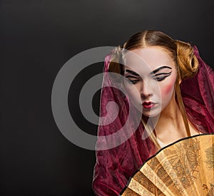 Girl in geisha costume with fan on black background