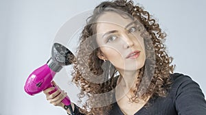 Girl Gets Her Hair Curly. Hair care concept. A curly woman dries her hair at home with a hair dryer with a diffuser