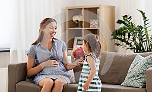 Girl giving flowers to her pregnant mother at home