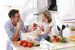 Girl giving a tomato to her father looking in kitchen photo
