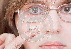 Girl with glasses holds contact lens