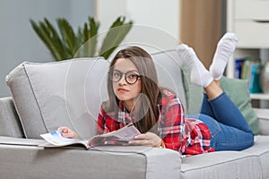 Girl in glasses listening music from smartphone with headphones in the living room at home.