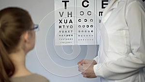 Girl in glasses looking at table letters, eyesight examination, ophthalmologist