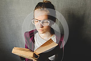 Girl with glasses reads a book. The girl is holding an old book