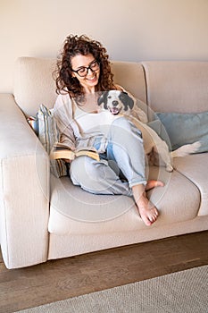 Girl in glasses sitting on sofa in living room with her young black and white dog