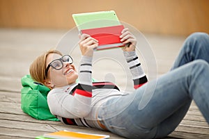 Girl in glasses and Tablet lies on wooden floor