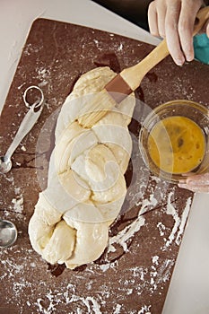 Girl glazing plaited challah dough with mum, overhead close up