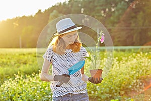 Girl in gloves with gardening tools planting flowers in garden