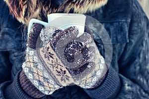 Girl in gloves holding cup of tea, white snowy background