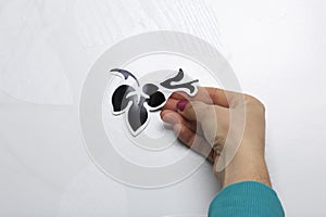 The girl glues the cut out elements from self-adhesive paper, to mask the defects of the white door.