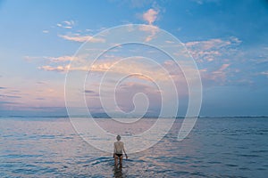 A girl goes swimming in the sea in the evening at sunset. Sunset on Sanur beach in Bali. Sunset sky and reflections of