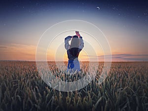 Girl in the golden wheat field at sunset. Beautiful twilight scenery under the summer starry sky with crescent moon. Magical