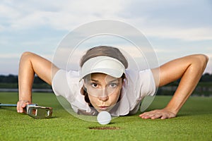 Girl golf player blowing ball into cup.