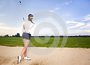 Girl golf player in bunker chipping ball.