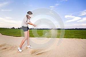 Girl golf player chipping ball in bunker.