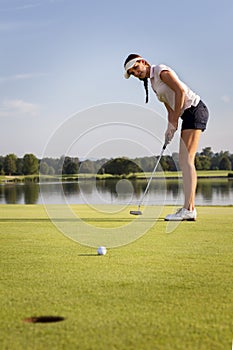 Girl golfer putting ball on green.