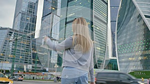 The girl is in a good mood walking through the city in the center of the city against the backdrop of skyscrapers and