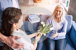 The girl and grandfather giving flowers and a gift to a grandmother.