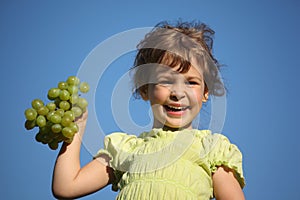 Girl with grape against blue sky