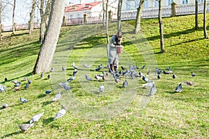 A girl in a gray coat feeds a flock of pigeons