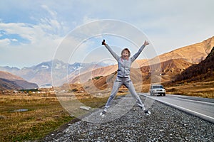 Girl in gray sports clothes on the road in the mountains on a summer or autumn day. A tourist is resting on a trip in nature