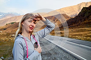 Girl in gray sports clothes on the road in the mountains on a summer or autumn day. A tourist is resting on a trip in nature