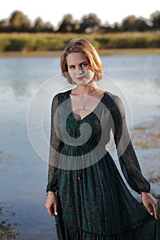 The girl in a green authentic dress walks at sunset on the coast of a reservoir