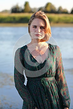 The girl in a green authentic dress walks at sunset on the coast of a reservoir