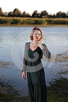 The girl in a green authentic dress walks at sunset on the coast of a reservoir